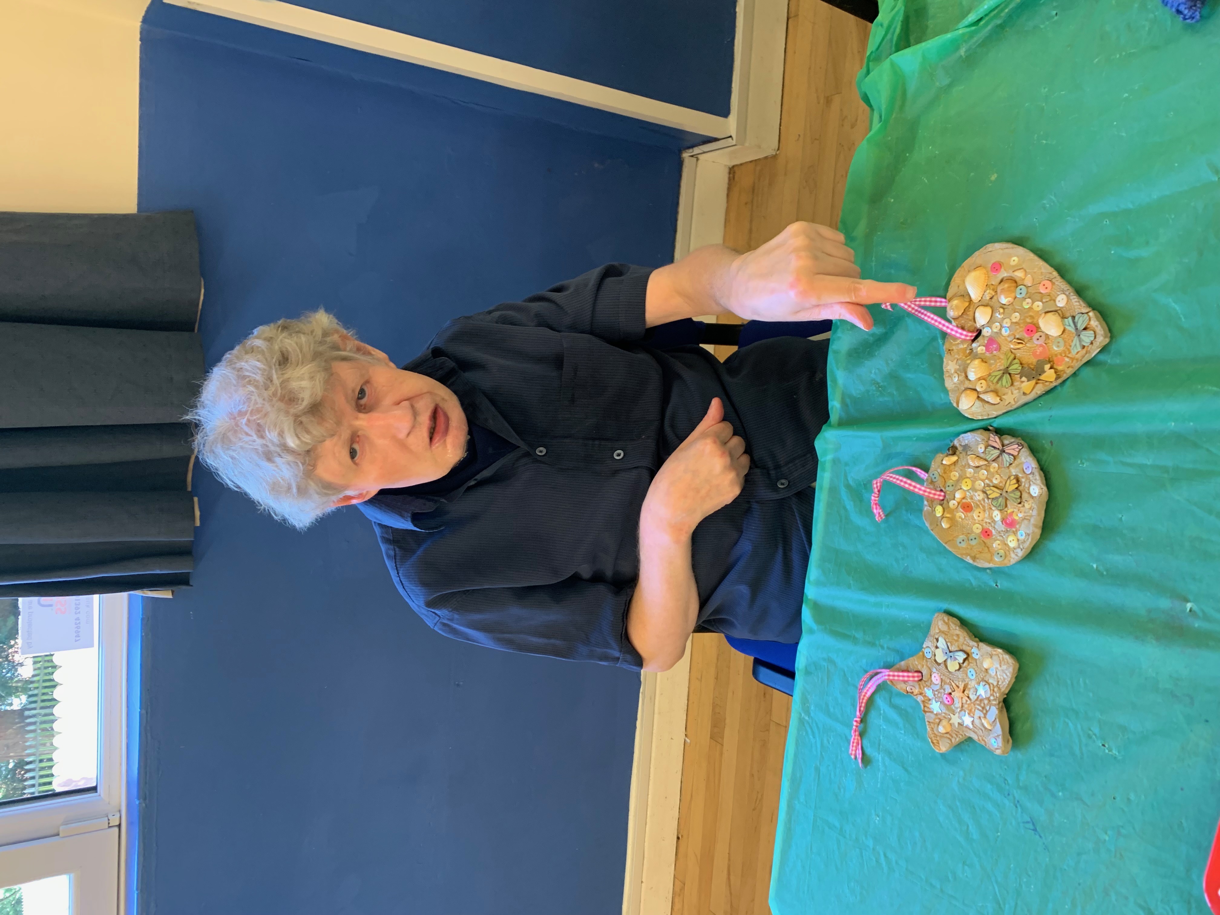 Participant proudly showing decorative clay ornaments with beads and ribbons