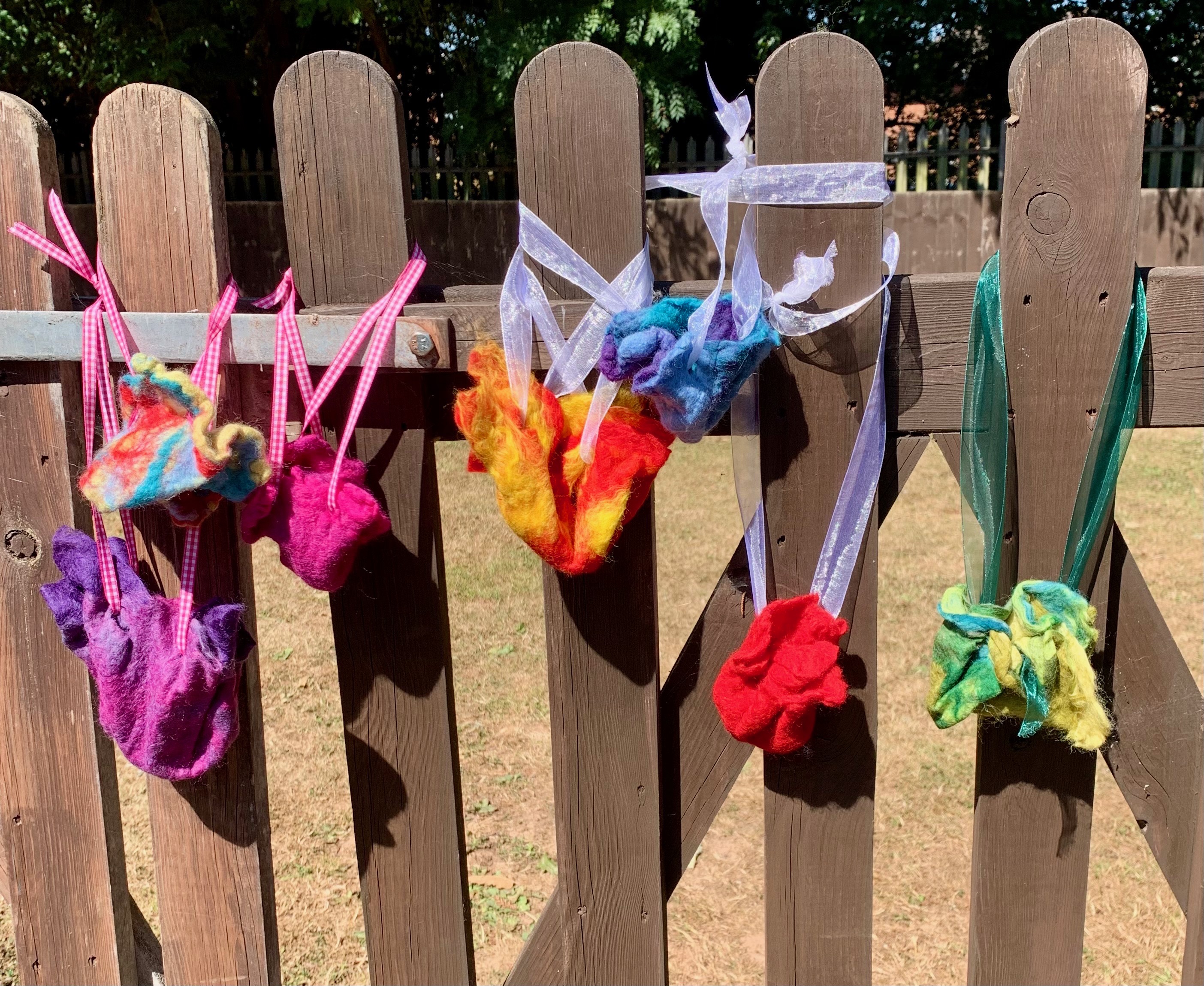 Colorful felt flowers hanging on wooden fence with ribbons