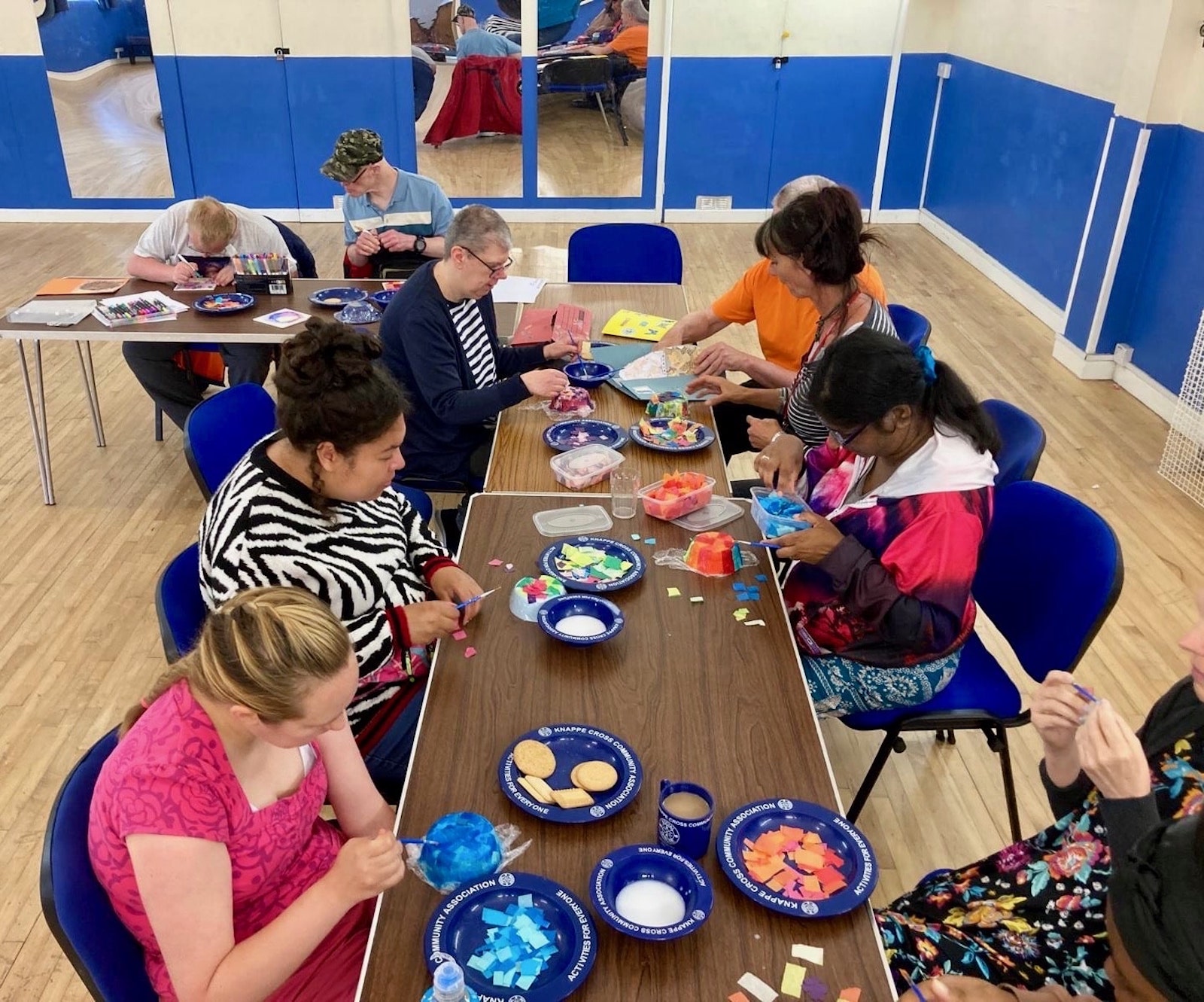 Multiple participants working together on art projects around tables with paint and materials