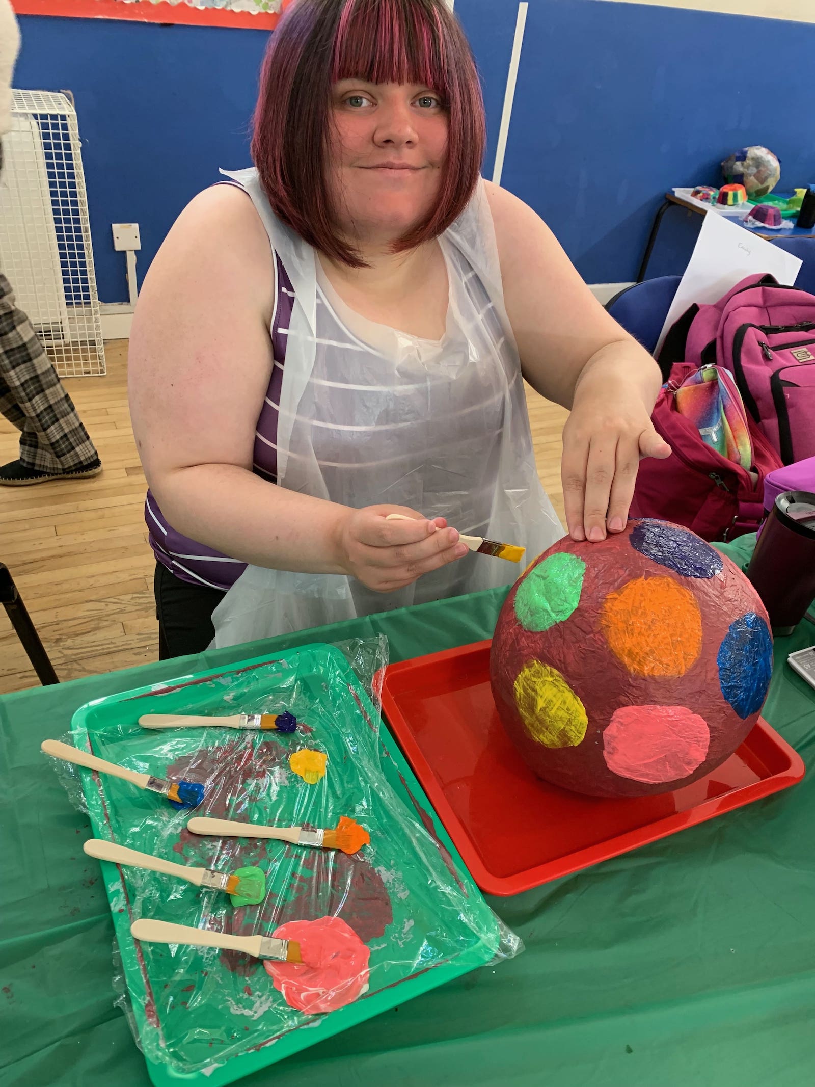 Participant painting colorful circles on spherical object with brushes and paint palette